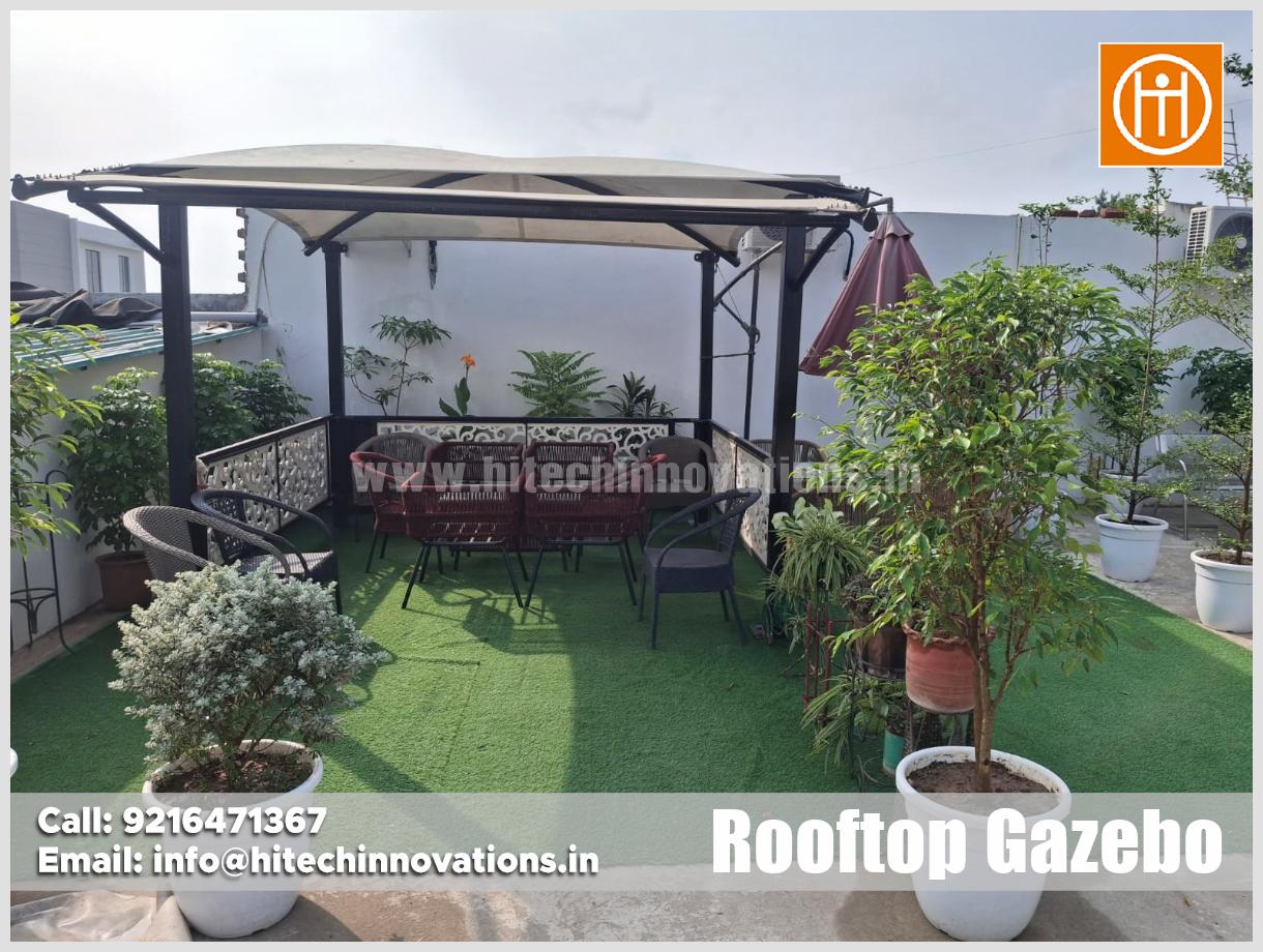 Luxurious rooftop gazebo by Hitech Innovations featuring white sheer curtains, warm lighting, wooden wall paneling, and a complete outdoor sofa set.