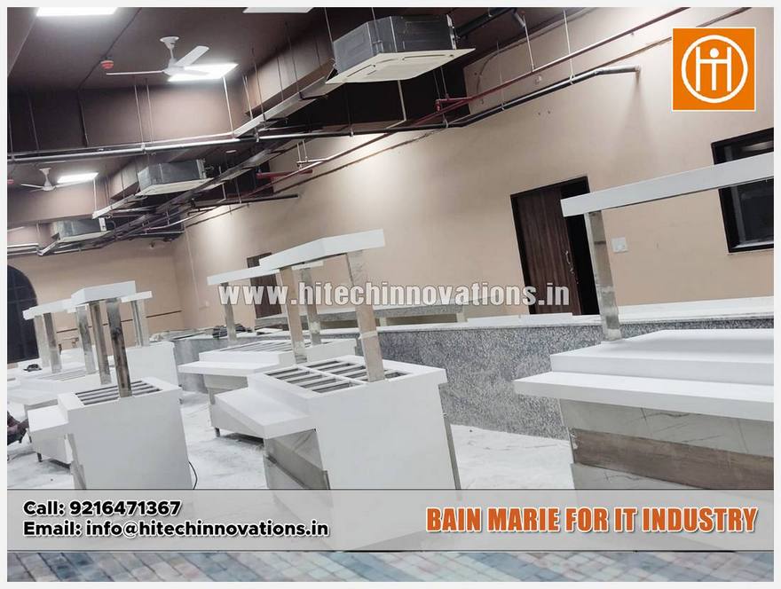 A wide-angle view of a large commercial cafeteria under construction, featuring multiple white Bain-Marie food service stations with overhead lighting and stainless steel supports