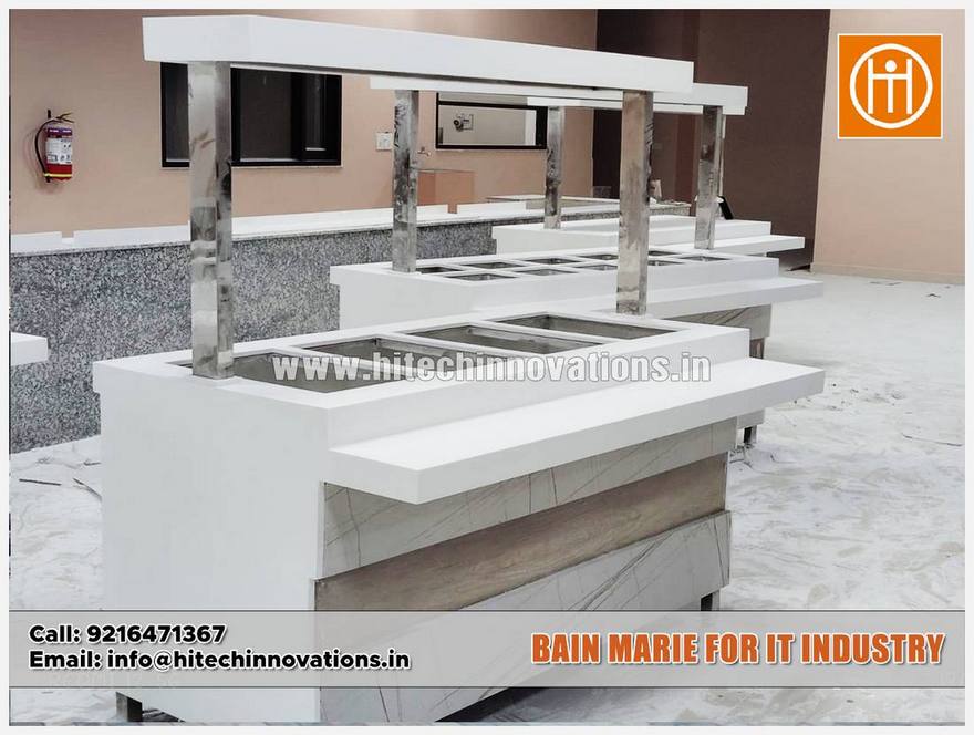 A high-angle shot of a white Bain-Marie station showing three deep stainless steel food warming pans and a multi-tiered Corian-style countertop