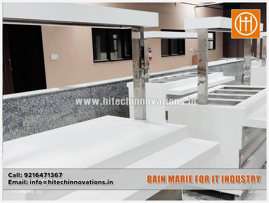 Close-up of a custom-built Bain-Marie counter with a clean white finish, featuring polished stainless steel pillars and an integrated sneeze guard or light fixture