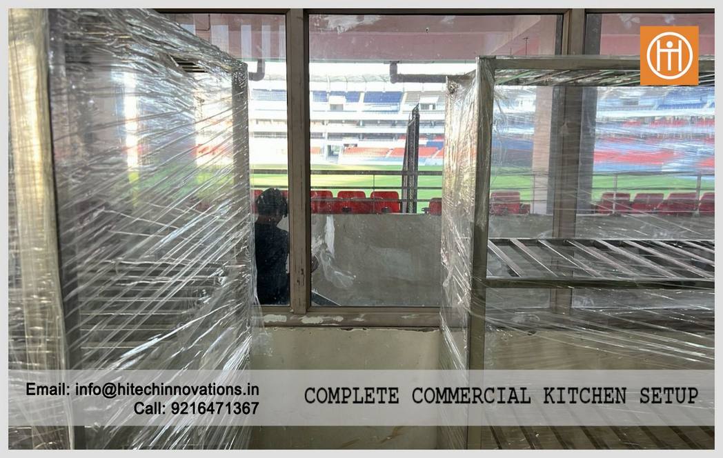 Stainless steel storage racks in a commercial kitchen setup overlooking the Maharaja Yadavindra Singh PCA Stadium seating area.