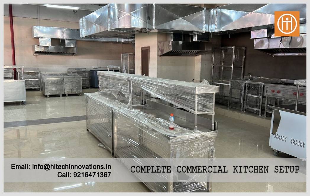 Central island work tables and overhead ventilation ducting in a large-scale commercial kitchen setup by Hitech Innovations