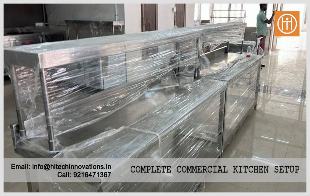 Row of stainless steel worktables and service counters with protective film, part of a complete commercial kitchen installation at PCA Stadium.