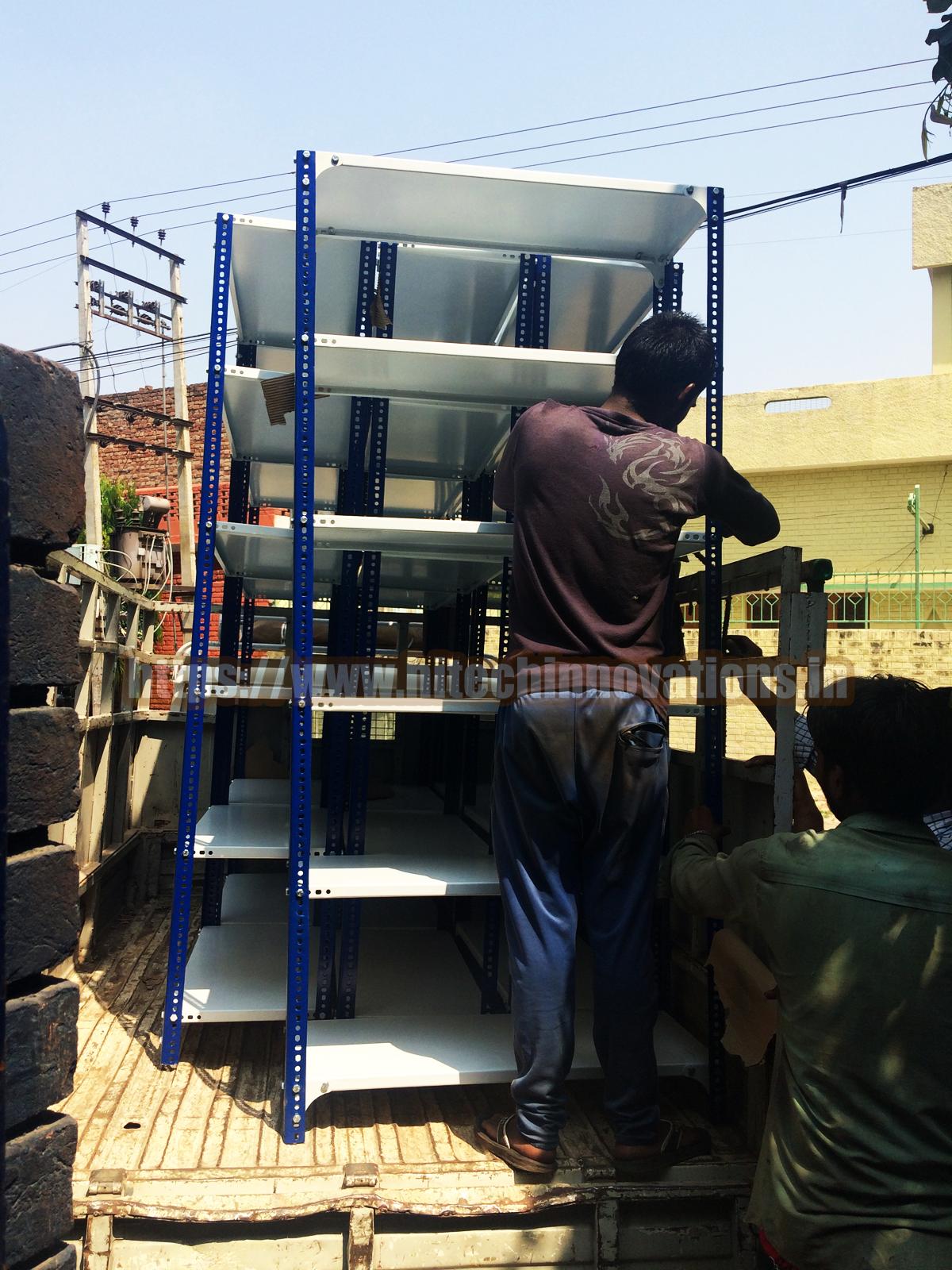 Workers loading fully assembled metal storage racks onto a delivery truck for industrial warehouse supply and logistical equipment transport.