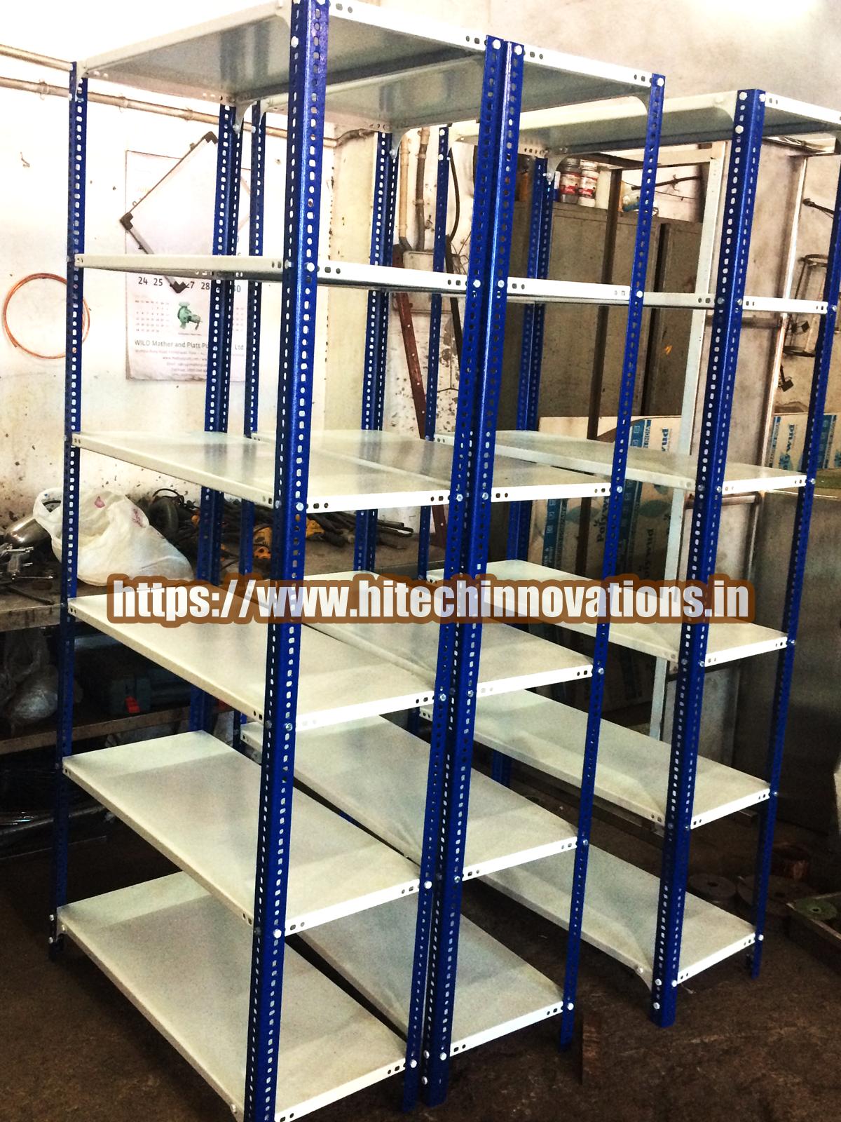 Heavy-duty industrial slotted angle storage racks with blue powder-coated pillars and adjustable white steel shelves for warehouse organization.