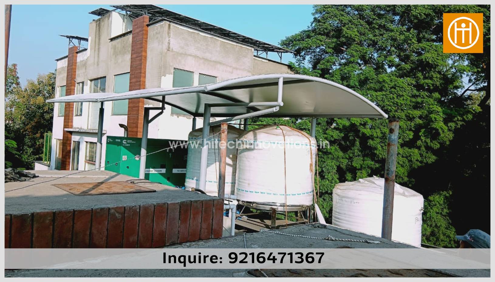 A high-angle view of a white, arch-shaped tensile shade structure by Hitech Innovations, providing overhead coverage for industrial water tanks and a generator on a rooftop facility.