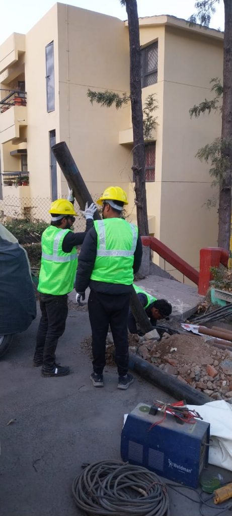 Skilled Hitech Innovations workers in safety gear erecting a heavy-duty steel support column for a tensile car parking structure.