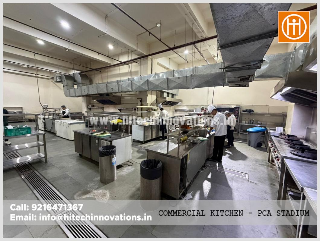 Wide angle view of a commercial kitchen setup by Hitech Innovations featuring heavy-duty exhaust hoods, food prep stations, and industrial flooring drainage.