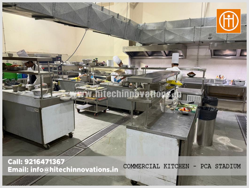 Chefs working at custom Hitech Innovations stainless steel workstations with integrated shelving and overhead ventilation systems.