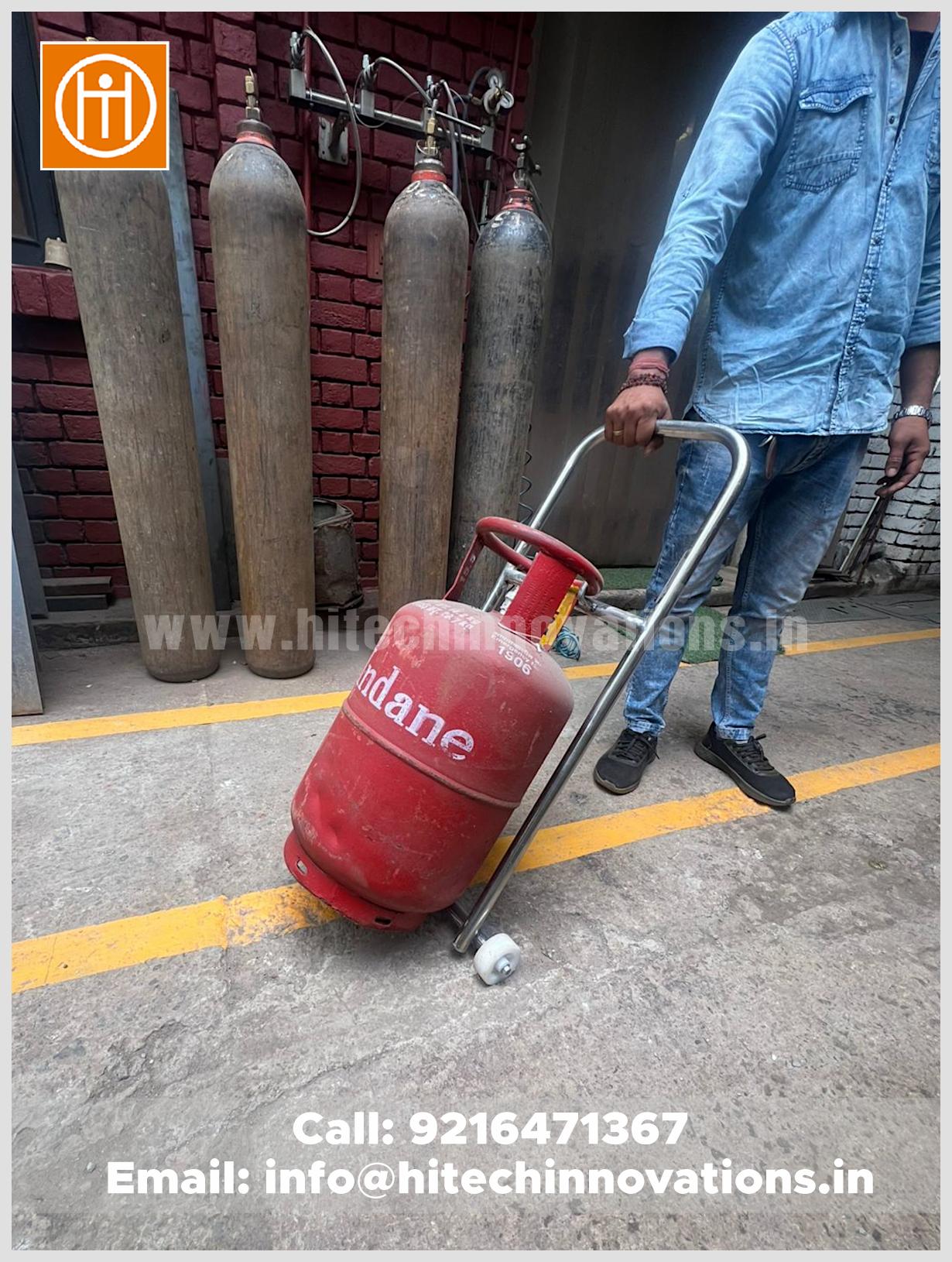Worker using a heavy duty iron gas cylinder trolley with wheels to move a red Indane LPG tank in an industrial workshop.