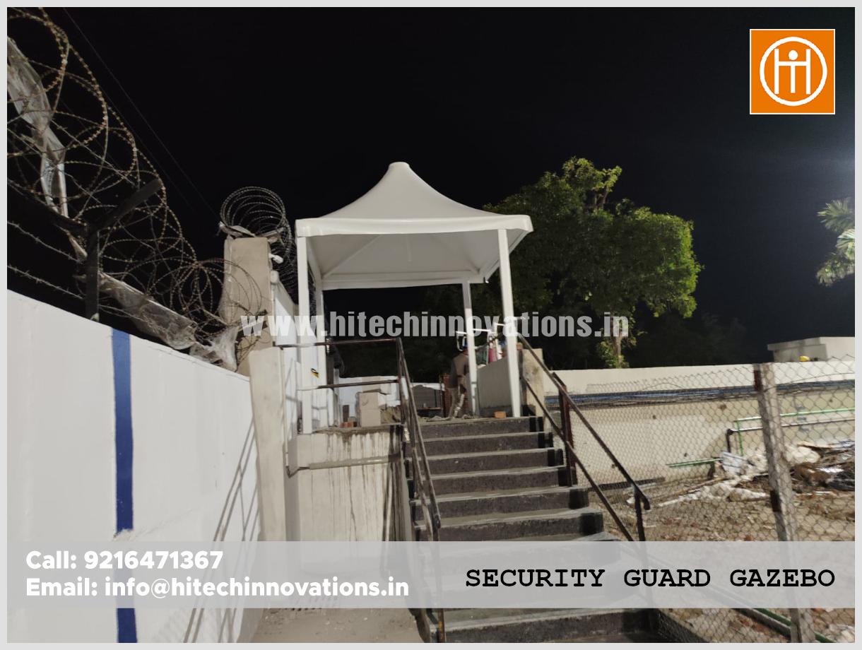 Finished white modern security guard gazebo installed at a secure industrial entrance at night.