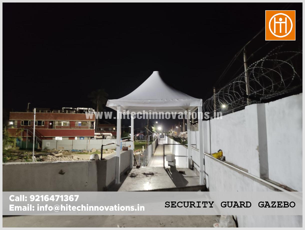 Wide angle view of a security gazebo overlooking a fenced industrial walkway at night.