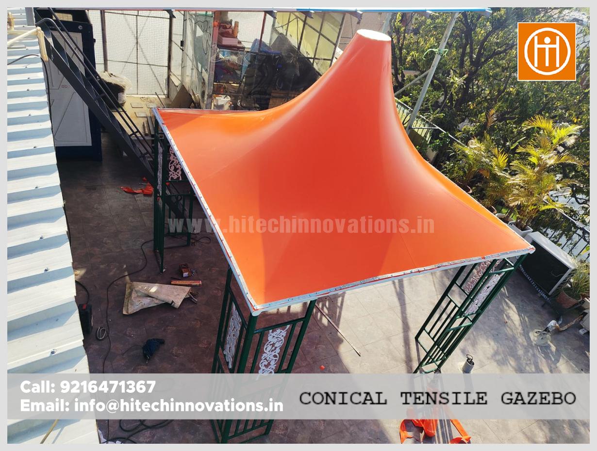Bird's eye view of a modern orange tensile structure with a conical peak and green support pillars.