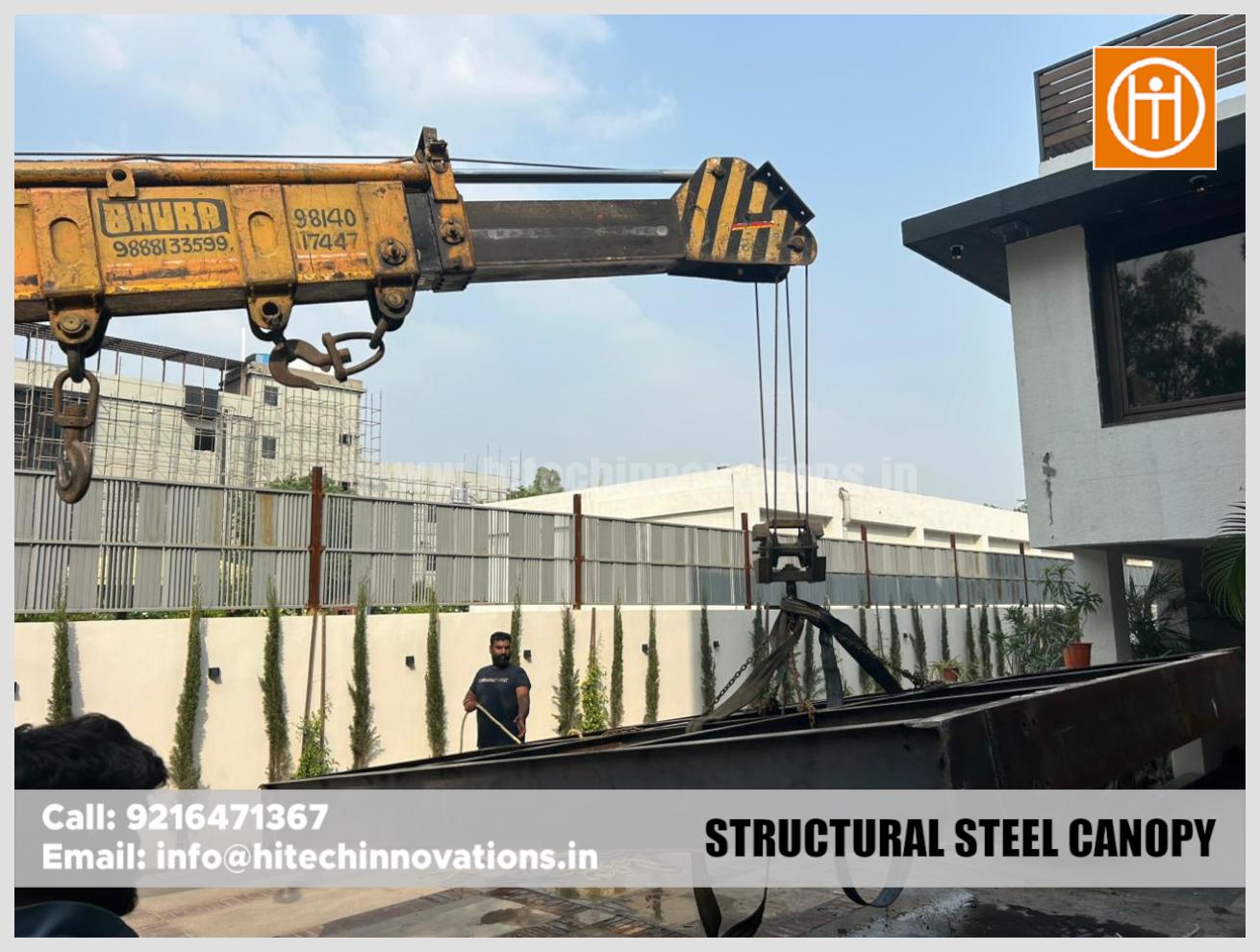 Worker guiding a large steel beam suspended by a crane during canopy construction.