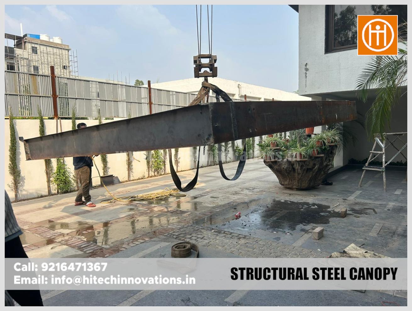 A construction worker guiding a heavy steel canopy frame suspended by a crane during installation.