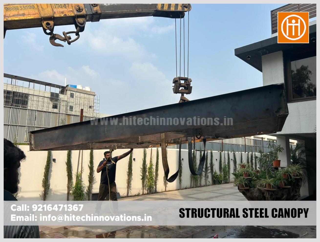 A crane lifting a structural steel canopy frame on a residential construction site.
