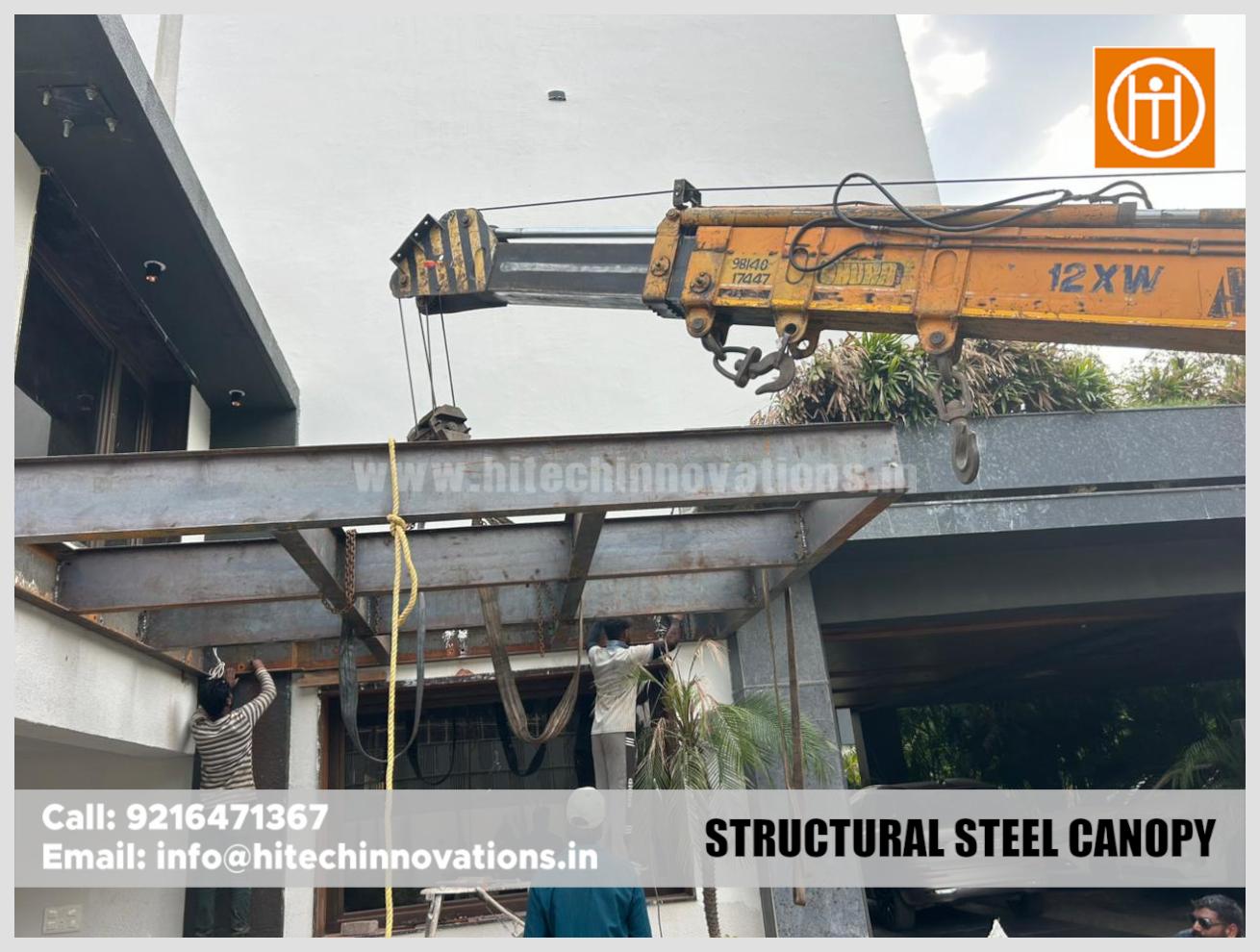 Construction workers securing a structural steel canopy frame to a building facade.