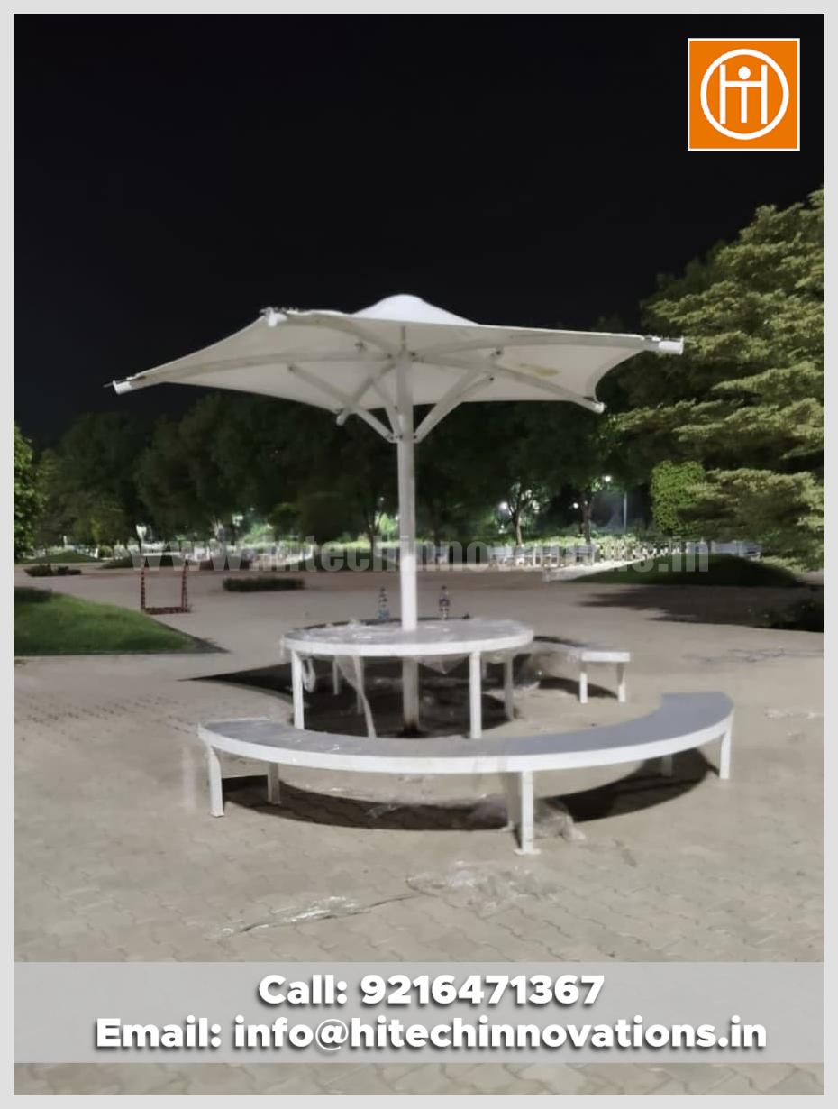 A top quality tensile conical umbrella installed outdoors at Lovely Professional University, featuring attached seating and tables for students.