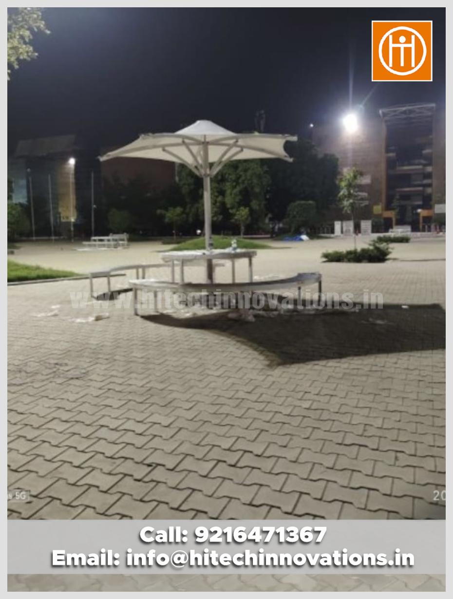 A wide view of a white tensile conical umbrella structure with outdoor seating at night on a university campus.