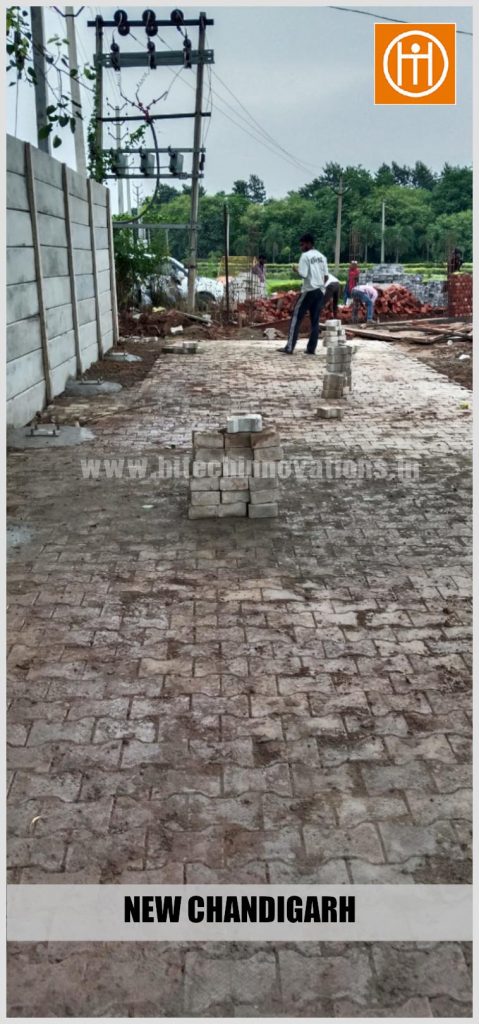 Ground preparation and interlocking paver block installation alongside boundary walls for the New Chandigarh project site.