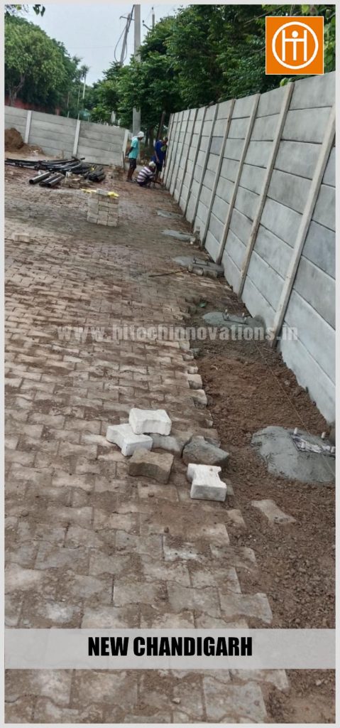 Construction workers aligning paver blocks and preparing column base markings along the perimeter wall.