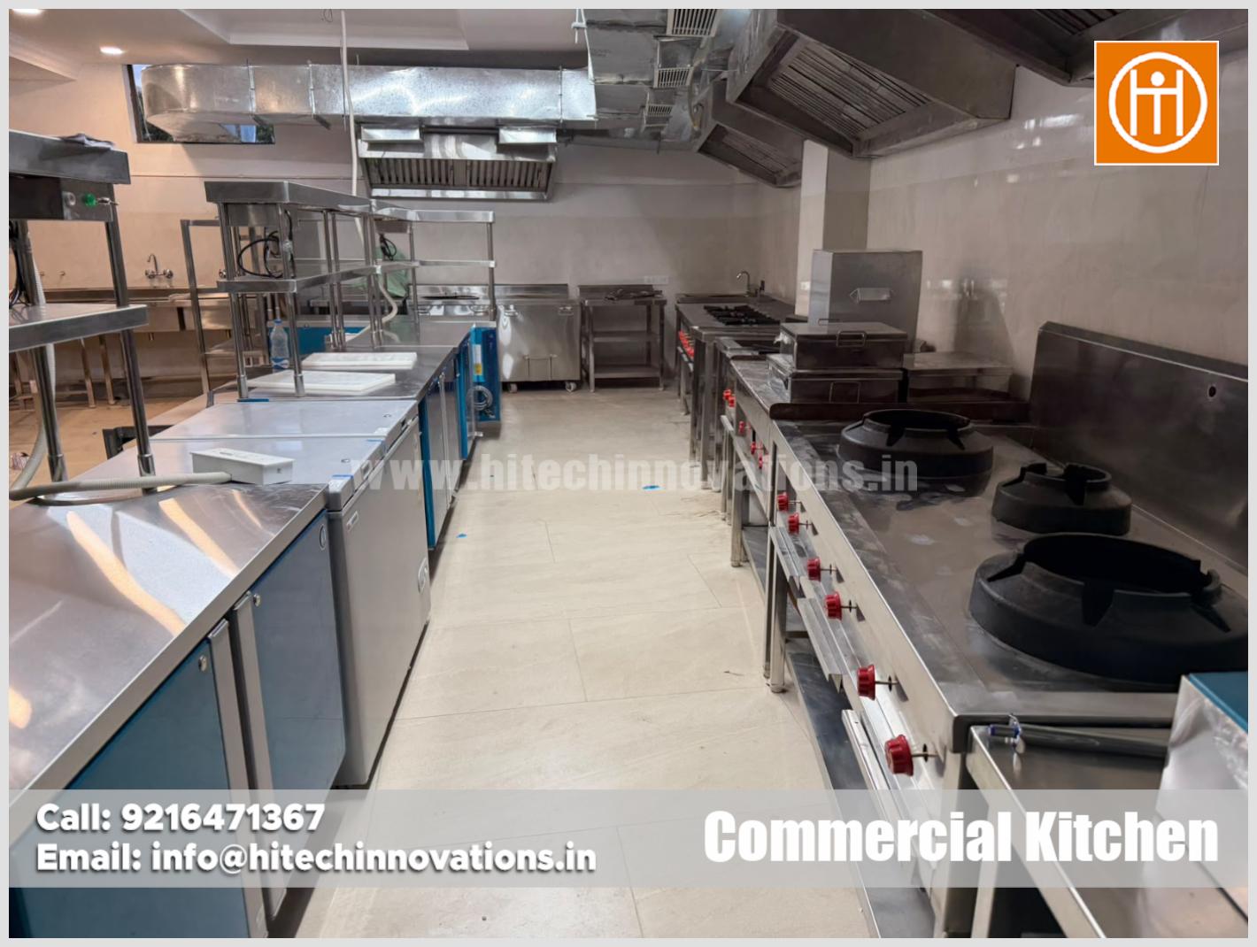 Complete stainless steel commercial kitchen setup with gas burners, undercounter chillers, and exhaust hoods by Hitech Innovations